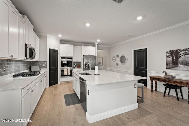 75013 Pondside Ln, Yulee, FL 32097 - kitchen with appliances with stainless steel finishes, ornamental molding, light wood-style floors, a large island with sink, and decorative backsplash
