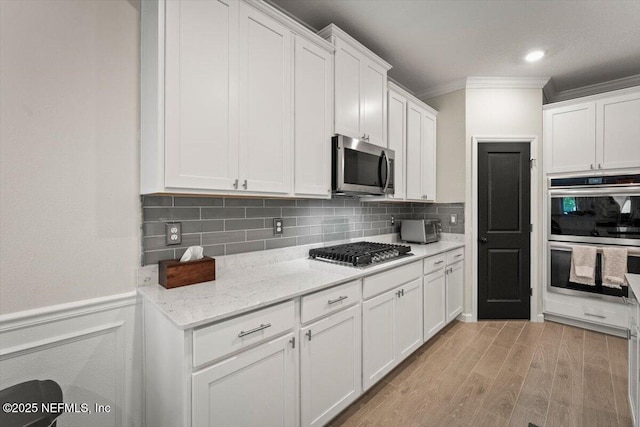 75013 Pondside Ln, Yulee, FL 32097 - kitchen with stainless steel appliances, crown molding, white cabinetry, light wood-style flooring, and decorative backsplash
