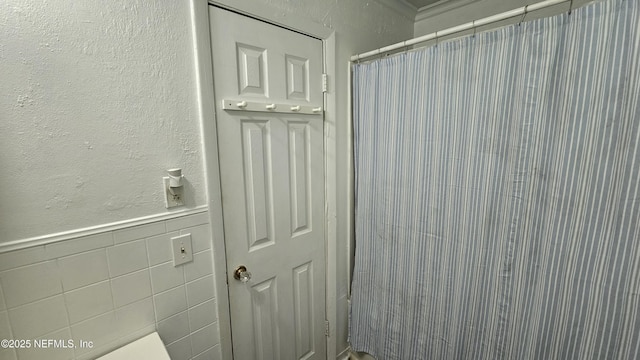 1319 Hickory St, Fernandina Beach, FL 32034 - bathroom featuring wainscoting, a shower with shower curtain, a textured wall, and tile walls