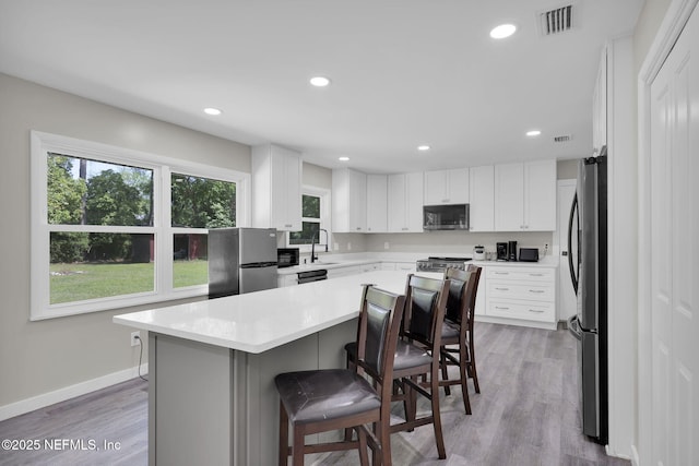11707 Village Ln, Jacksonville, FL 32223 - kitchen featuring appliances with stainless steel finishes, a kitchen breakfast bar, light countertops, white cabinets, and a kitchen island