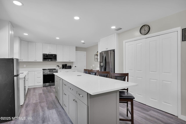 11707 Village Ln, Jacksonville, FL 32223 - kitchen with stainless steel appliances, a breakfast bar area, wood finished floors, a center island, and white cabinetry