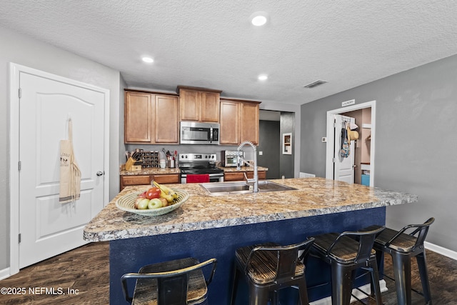2264 Pebble Point Dr, Green Cove Springs, FL 32043 - kitchen featuring appliances with stainless steel finishes, an island with sink, brown cabinets, a textured ceiling, and a kitchen breakfast bar