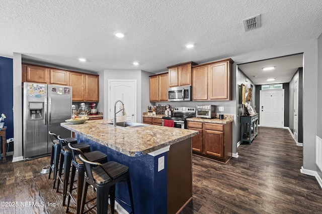 2264 Pebble Point Dr, Green Cove Springs, FL 32043 - kitchen featuring appliances with stainless steel finishes, dark wood-style floors, an island with sink, light countertops, and brown cabinetry