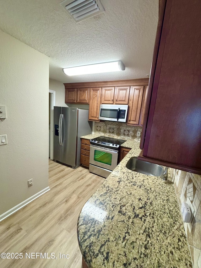 7701 Timberlin Park Blvd Unit 322, Jacksonville, FL 32256 - kitchen featuring stainless steel appliances, light wood-style floors, backsplash, brown cabinets, and a textured ceiling