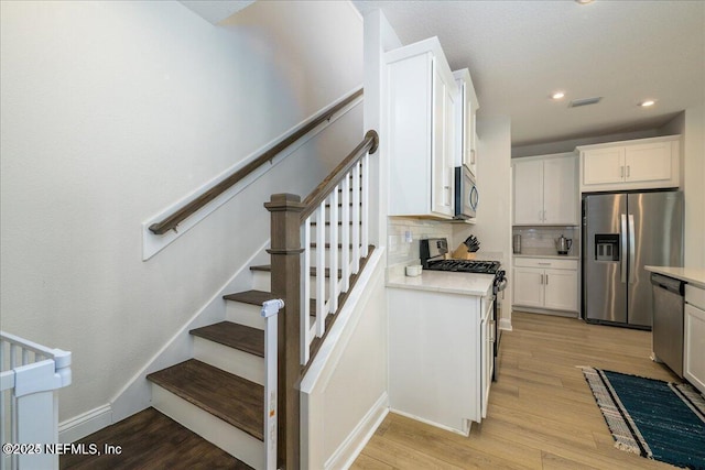 143 Dahlia Falls Dr, Saint Johns, FL 32259 - kitchen with stainless steel appliances, light countertops, backsplash, light wood finished floors, and white cabinets