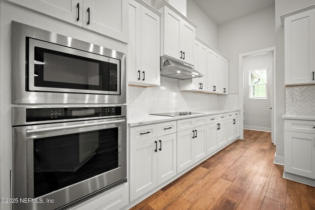36250 Pitch Ln, Hilliard, FL 32046 - kitchen featuring appliances with stainless steel finishes, under cabinet range hood, backsplash, white cabinetry, and light wood-style flooring