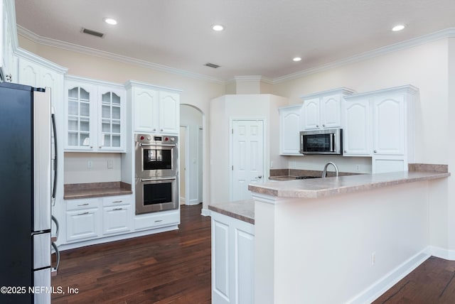 1700 Southcreek Dr, Saint Johns, FL 32259 - kitchen with stainless steel appliances, dark wood-style floors, white cabinetry, a peninsula, and glass insert cabinets