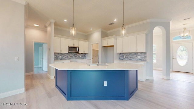 99 Sloganeer Trl, Palm Coast, FL 32164 - kitchen featuring stainless steel microwave, white cabinets, tasteful backsplash, a large island with sink, and crown molding