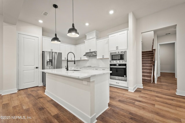 36258 Pitch Ln, Hilliard, FL 32046 - kitchen featuring appliances with stainless steel finishes, under cabinet range hood, white cabinetry, decorative backsplash, and an island with sink