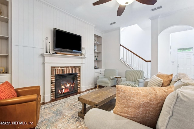 85488 Sagaponack Dr, Fernandina Beach, FL 32034 - living room with built in shelves, a ceiling fan, ornamental molding, wood finished floors, and a fireplace
