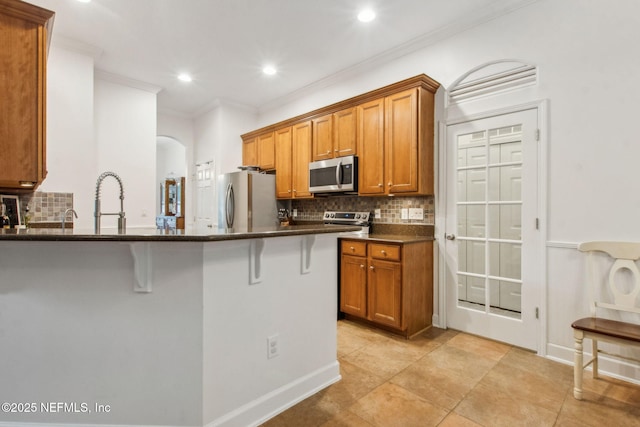 85488 Sagaponack Dr, Fernandina Beach, FL 32034 - kitchen featuring stainless steel appliances, brown cabinetry, decorative backsplash, a breakfast bar, and arched walkways