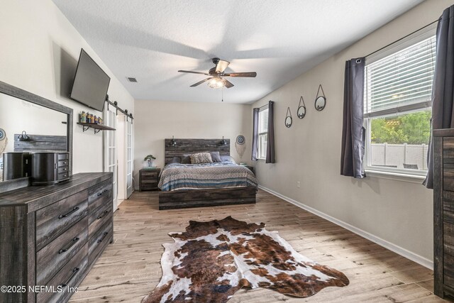 3299 Hidden Meadows Ct, Green Cove Springs, FL 32043 - bedroom with a barn door, light wood-style floors, a ceiling fan, and a textured ceiling