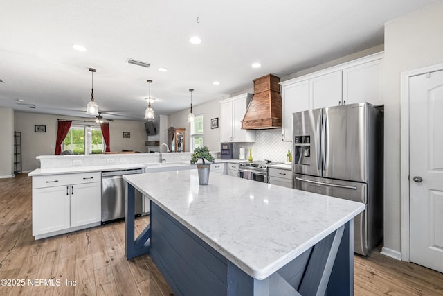 3299 Hidden Meadows Ct, Green Cove Springs, FL 32043 - kitchen featuring appliances with stainless steel finishes, custom range hood, a peninsula, light wood-style floors, and light stone countertops