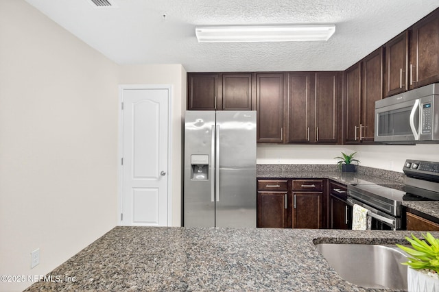 218 Larkin Pl Unit 105, Saint Johns, FL 32259 - kitchen with stainless steel appliances, dark brown cabinetry, a textured ceiling, and dark stone counters