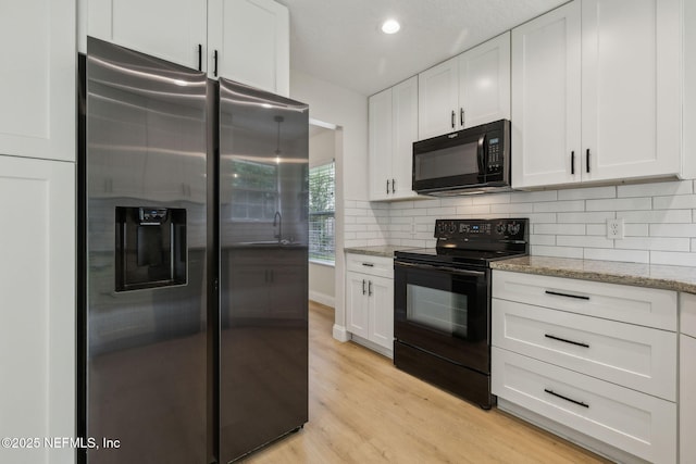 4804 Winton Cir, Saint Augustine, FL 32086 - kitchen featuring black appliances, white cabinetry, light stone countertops, light wood-style flooring, and decorative backsplash