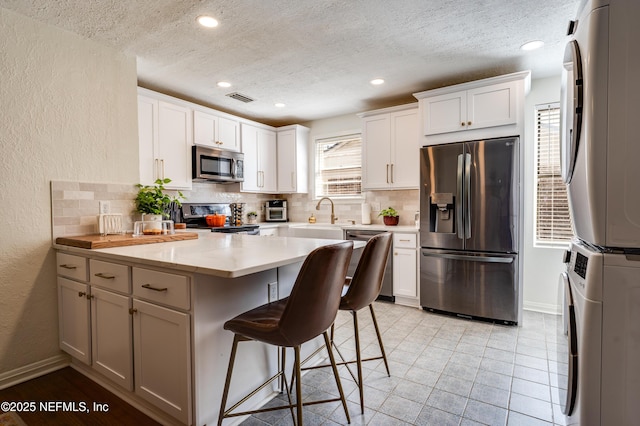 4818 Astral St, Jacksonville, FL 32205 - kitchen featuring appliances with stainless steel finishes, stacked washer / dryer, decorative backsplash, a textured wall, and a breakfast bar
