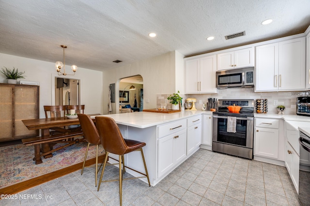 4818 Astral St, Jacksonville, FL 32205 - kitchen featuring appliances with stainless steel finishes, a peninsula, arched walkways, a textured ceiling, and decorative backsplash