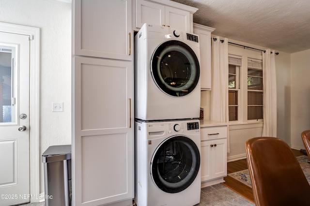 4818 Astral St, Jacksonville, FL 32205 - laundry area featuring stacked washer and clothes dryer, cabinet space, a textured ceiling, and wood finished floors