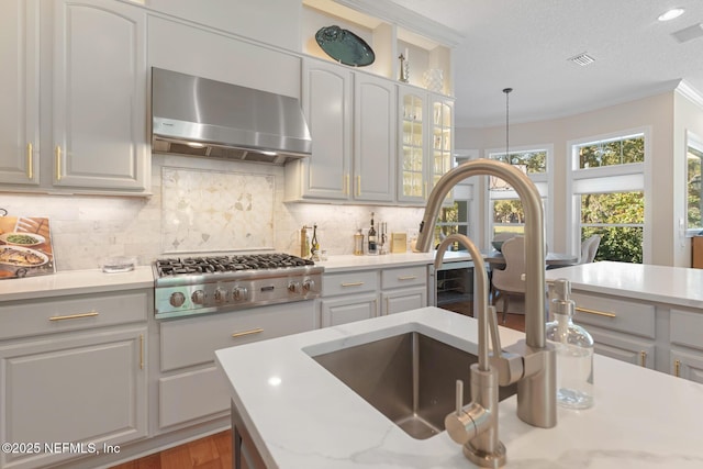 1614 Sheffield Park Ct, Jacksonville, FL 32225 - kitchen featuring wall chimney exhaust hood, stainless steel gas stovetop, backsplash, glass insert cabinets, and crown molding