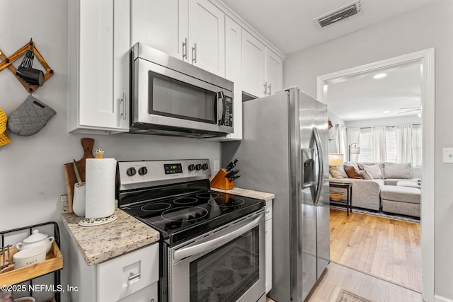 4737 College St, Jacksonville, FL 32205 - kitchen featuring appliances with stainless steel finishes, white cabinets, light wood finished floors, open floor plan, and light stone countertops