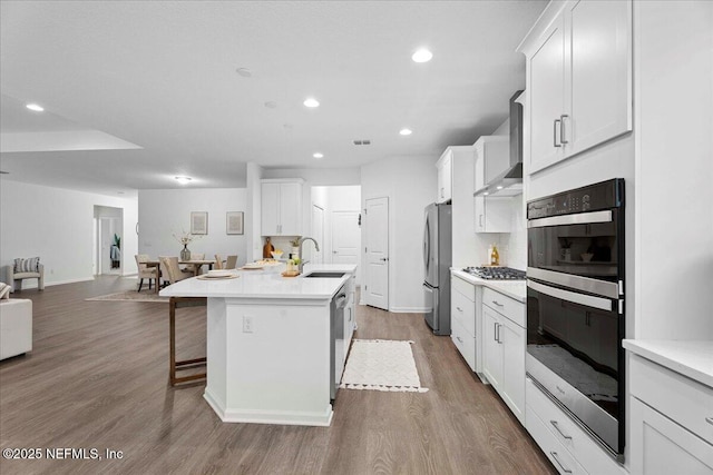 227 Wind Chime Ln, Saint Augustine, FL 32095 - kitchen featuring appliances with stainless steel finishes, wall chimney range hood, open floor plan, a center island with sink, and a kitchen breakfast bar