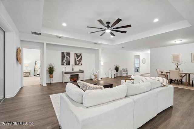 227 Wind Chime Ln, Saint Augustine, FL 32095 - living area featuring a tray ceiling, recessed lighting, a ceiling fan, dark wood-type flooring, and a lit fireplace