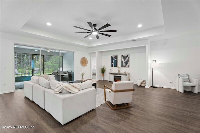 227 Wind Chime Ln, Saint Augustine, FL 32095 - living room featuring a tray ceiling, ceiling fan, recessed lighting, dark wood-style flooring, and a warm lit fireplace