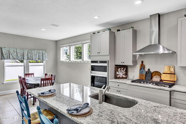 62 Seaside Vista Ct, Saint Augustine, FL 32084 - kitchen with wall chimney exhaust hood, appliances with stainless steel finishes, a breakfast bar, light stone counters, and light tile patterned floors