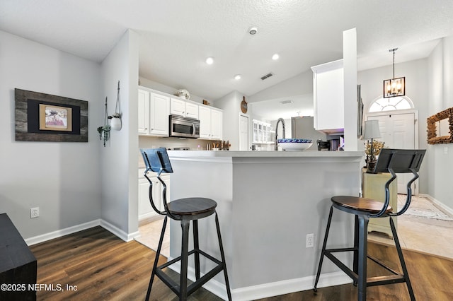 145 E Blackjack Branch Way, Saint Johns, FL 32259 - kitchen featuring stainless steel microwave, a breakfast bar area, white cabinets, dark wood-type flooring, and vaulted ceiling