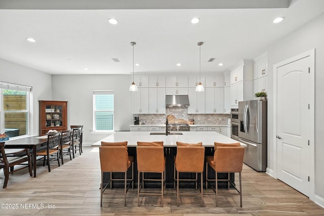 214 Gap Creek Dr, Saint Johns, FL 32259 - kitchen with under cabinet range hood, appliances with stainless steel finishes, light countertops, light wood finished floors, and a center island with sink
