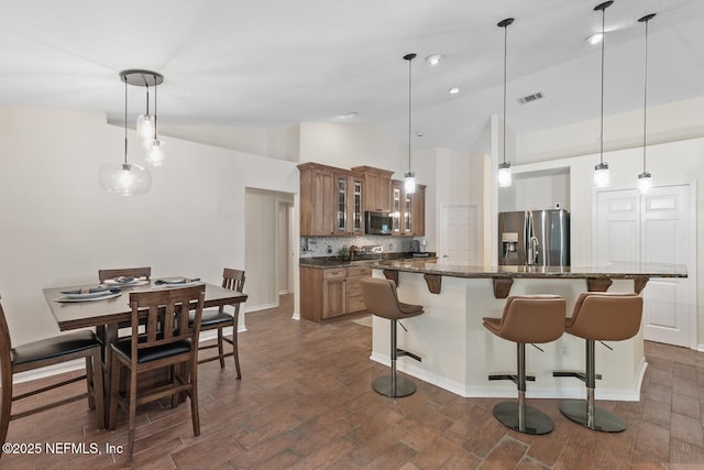 213 Seamist Ct, Ponte Vedra Beach, FL 32082 - kitchen with stainless steel appliances, brown cabinetry, vaulted ceiling, a kitchen breakfast bar, and decorative backsplash