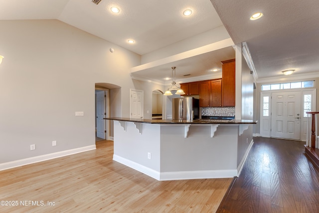 1300 Coopers Hawk Way, Middleburg, FL 32068 - kitchen with freestanding refrigerator, brown cabinets, a kitchen breakfast bar, arched walkways, and ornamental molding