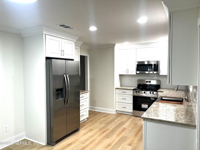523 Eloise St, Macclenny, FL 32063 - kitchen featuring appliances with stainless steel finishes, ornamental molding, white cabinets, light wood-style flooring, and backsplash