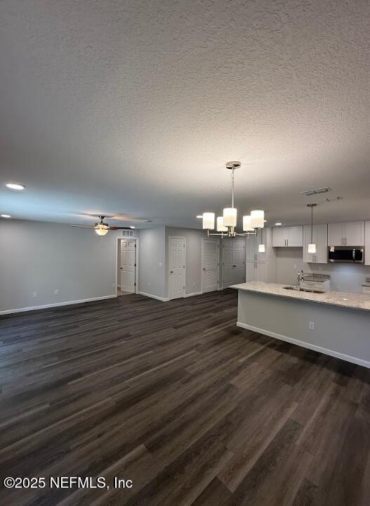 3138 Phyllis St, Jacksonville, FL 32205 - unfurnished living room featuring dark wood finished floors, a textured ceiling, a chandelier, and a ceiling fan