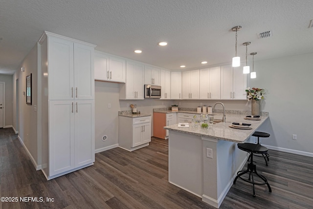 3138 Phyllis St, Jacksonville, FL 32205 - kitchen featuring stainless steel microwave, a peninsula, white cabinets, a breakfast bar area, and recessed lighting