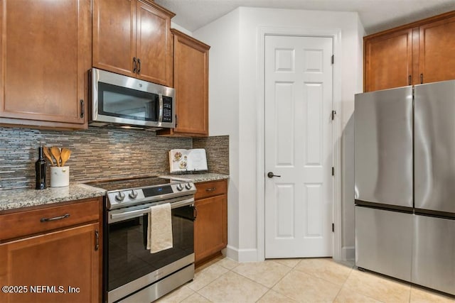 85212 Champlain Dr, Fernandina Beach, FL 32034 - kitchen with stainless steel appliances, light tile patterned floors, backsplash, light stone countertops, and brown cabinets
