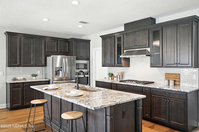 24 Tradesman Ln, Saint Johns, FL 32259 - kitchen with stainless steel appliances, exhaust hood, light wood-type flooring, a textured ceiling, and a center island with sink