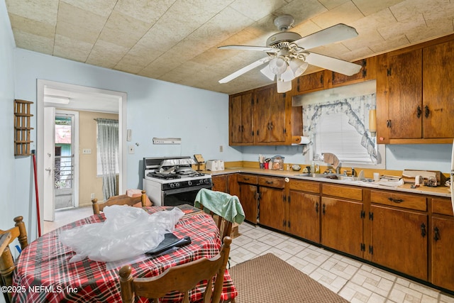 44125 Jarrett Rd, Callahan, FL 32011 - kitchen with range with gas cooktop, light countertops, brown cabinetry, a ceiling fan, and brick patterned floors