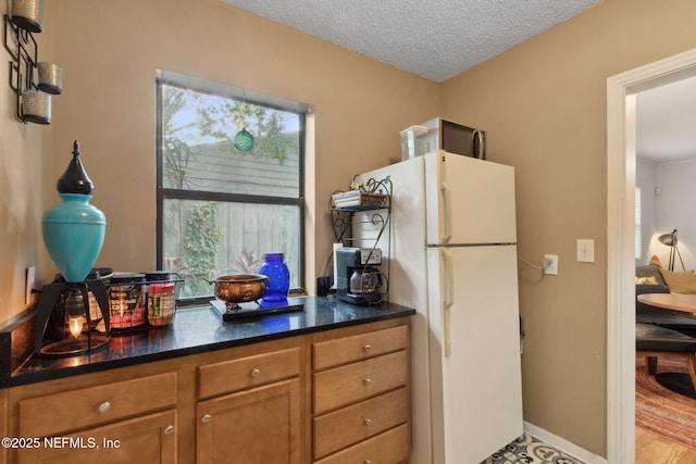 3207 Plum St, Jacksonville, FL 32205 - kitchen featuring freestanding refrigerator, brown cabinets, a textured ceiling, and dark stone counters