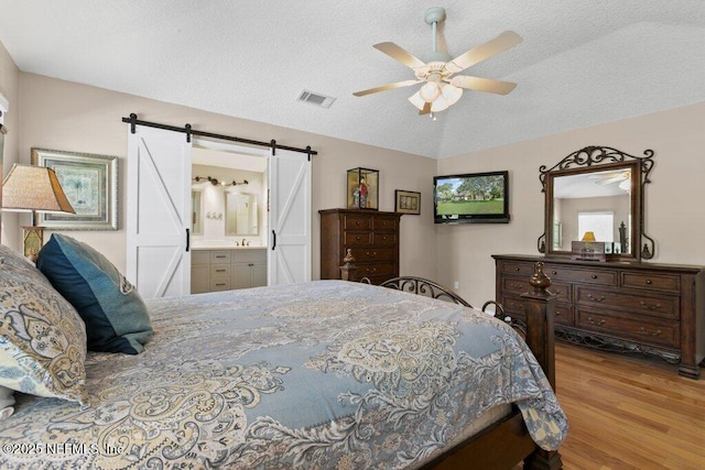 508 Lighthouse Ct, Neptune Beach, FL 32266 - bedroom featuring a barn door, wood finished floors, a textured ceiling, connected bathroom, and vaulted ceiling