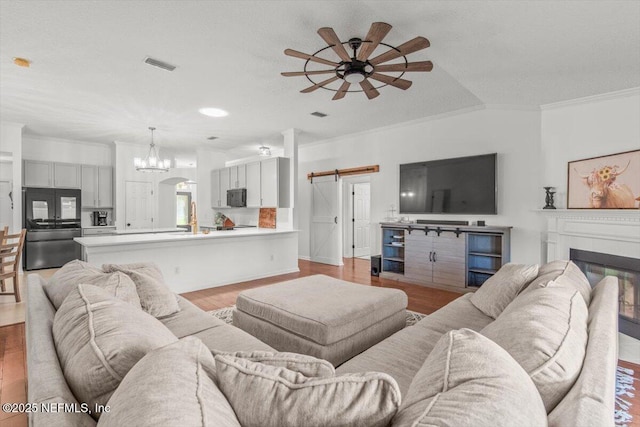 2484 Royal Pointe Dr, Green Cove Springs, FL 32043 - living room with a ceiling fan, a barn door, wood finished floors, crown molding, and a chandelier