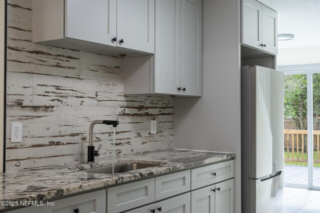 8305 Coralberry Ln, Jacksonville, FL 32244 - kitchen featuring freestanding refrigerator, decorative backsplash, light stone countertops, and white cabinets