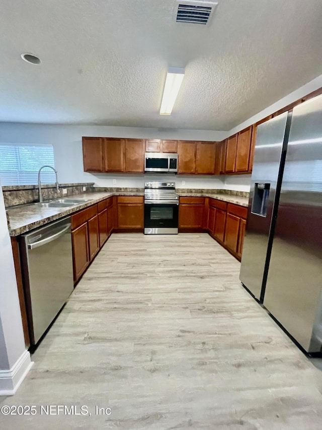 86069 Pineview Dr, Yulee, FL 32097 - kitchen featuring stainless steel appliances, light wood-style flooring, brown cabinets, and a textured ceiling