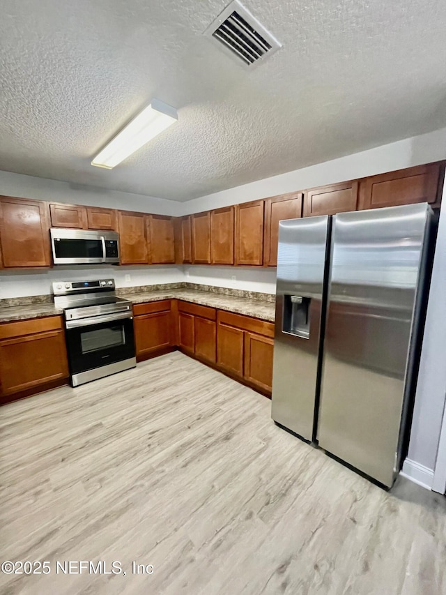 86069 Pineview Dr, Yulee, FL 32097 - kitchen featuring stainless steel appliances, a textured ceiling, light wood-type flooring, and brown cabinetry