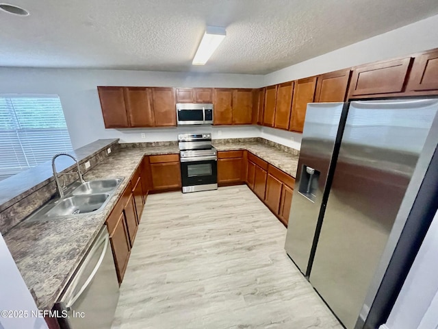 86069 Pineview Dr, Yulee, FL 32097 - kitchen featuring appliances with stainless steel finishes, a textured ceiling, a peninsula, brown cabinetry, and light wood-style floors