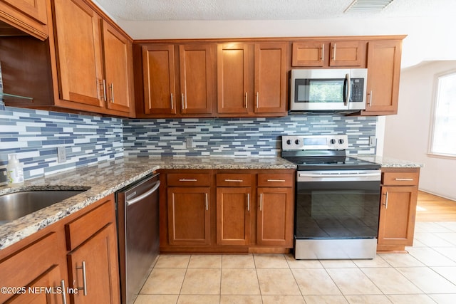 3312 Dellwood Ave, Jacksonville, FL 32205 - kitchen with stainless steel appliances, brown cabinets, backsplash, light stone countertops, and a textured ceiling