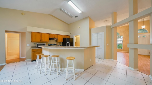 2109 Hovington Cir W, Jacksonville, FL 32246 - kitchen with stainless steel microwave, freestanding refrigerator, under cabinet range hood, high vaulted ceiling, and brown cabinetry
