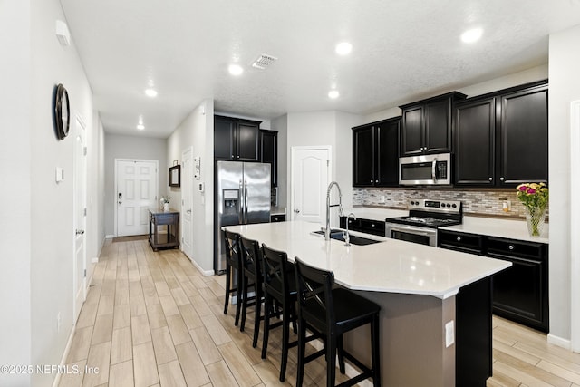9217 Gilmore Grove Way, Jacksonville, FL 32211 - kitchen with appliances with stainless steel finishes, dark cabinetry, light wood-style floors, tasteful backsplash, and a center island with sink