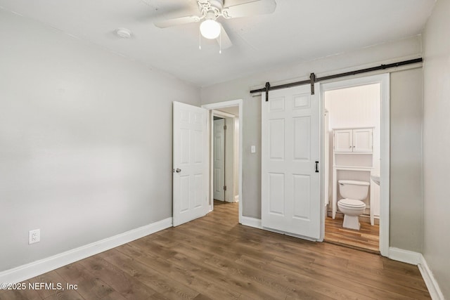 243 Ravenswood Dr, Saint Augustine, FL 32084 - unfurnished bedroom featuring a barn door, wood finished floors, connected bathroom, and ceiling fan