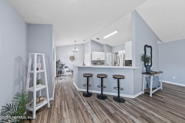 13254 Karla Cove Ln, Jacksonville, FL 32225 - kitchen with stainless steel fridge with ice dispenser, vaulted ceiling, white cabinets, dark wood-style flooring, and a breakfast bar